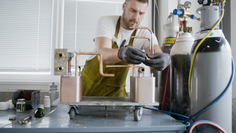 Man wearing apron and gloves works on a heat pump in a lab environment