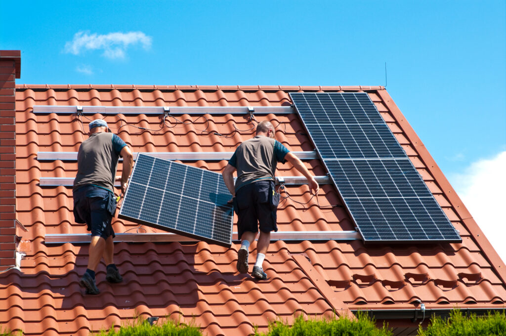 A man holding a solar panel walking up a roof